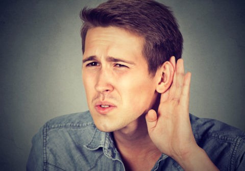 hard of hearing man placing hand on ear asking someone to speak up or listening to bad news, isolated on gray background. Negative emotion facial expression feeling