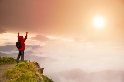 Young man with backpack standing on top of mountain watching the sunrise