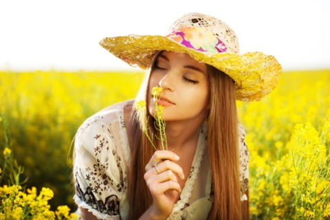Happy girl in a hat enjoying the smell of the flower